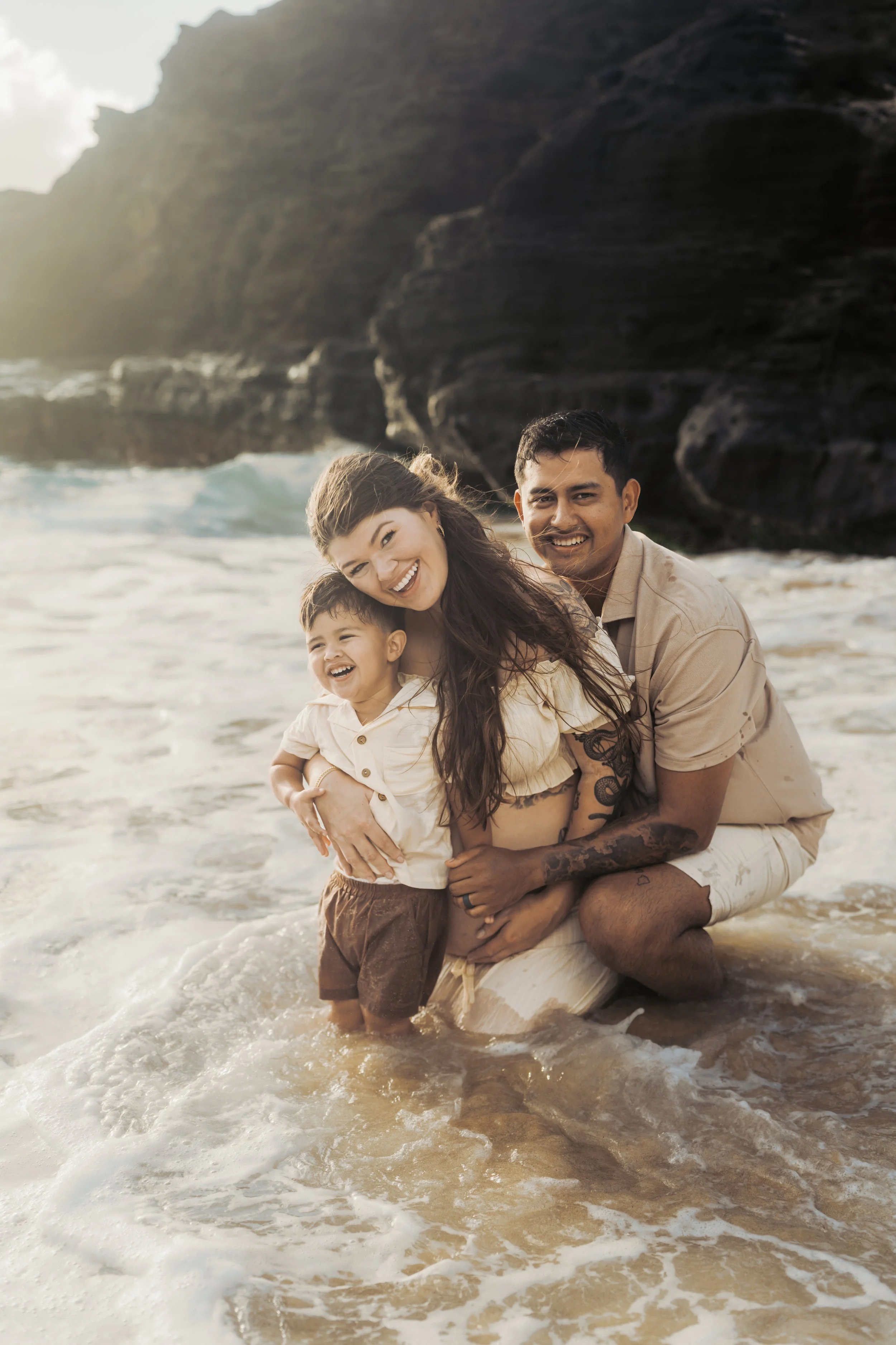 Family cuddles up in waves at iconic Halona Beach cove on island of Oahu for family maternity photo session