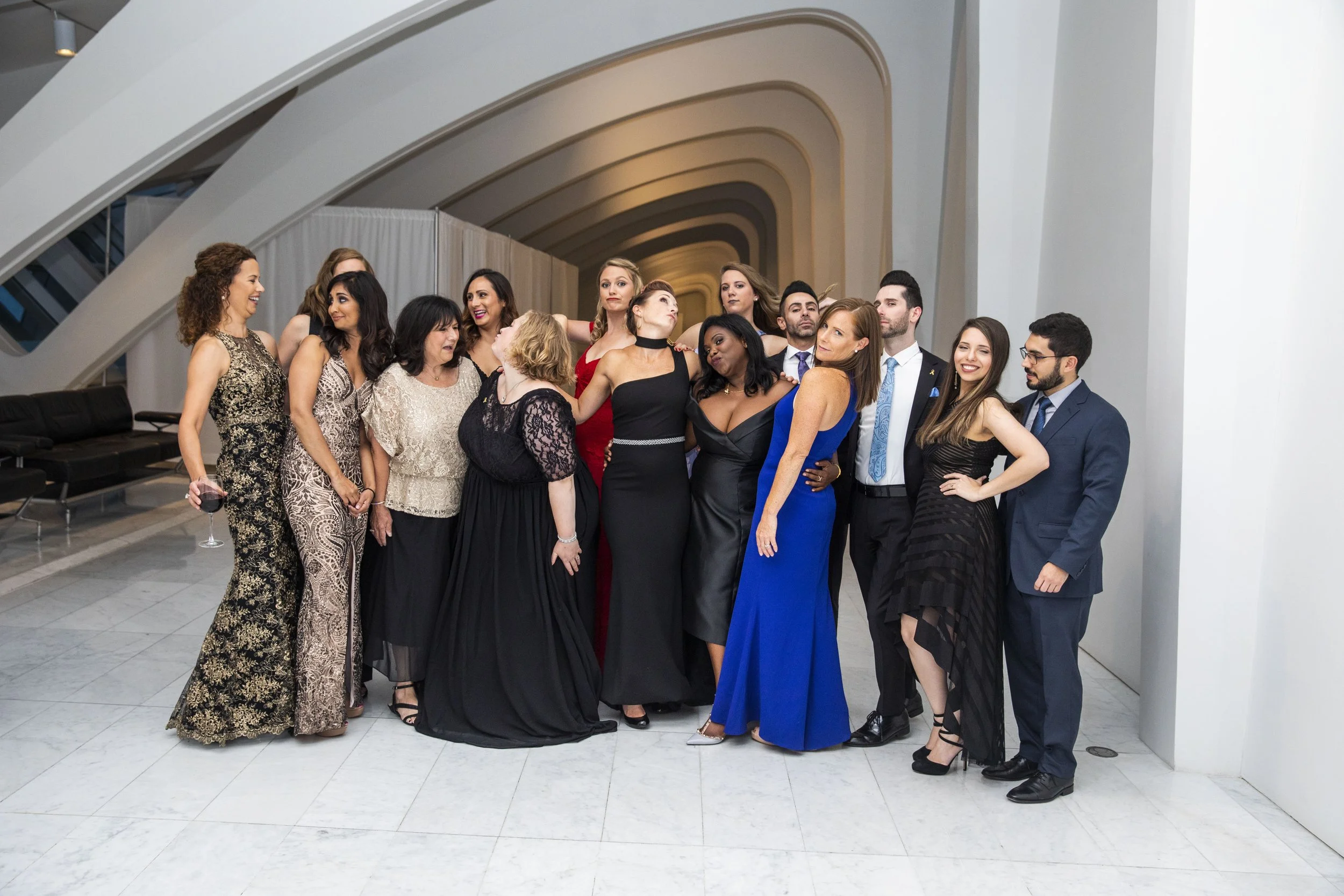 Group of well-dressed people at a formal event in a modern building with curved architectural design, posing together for a photo.