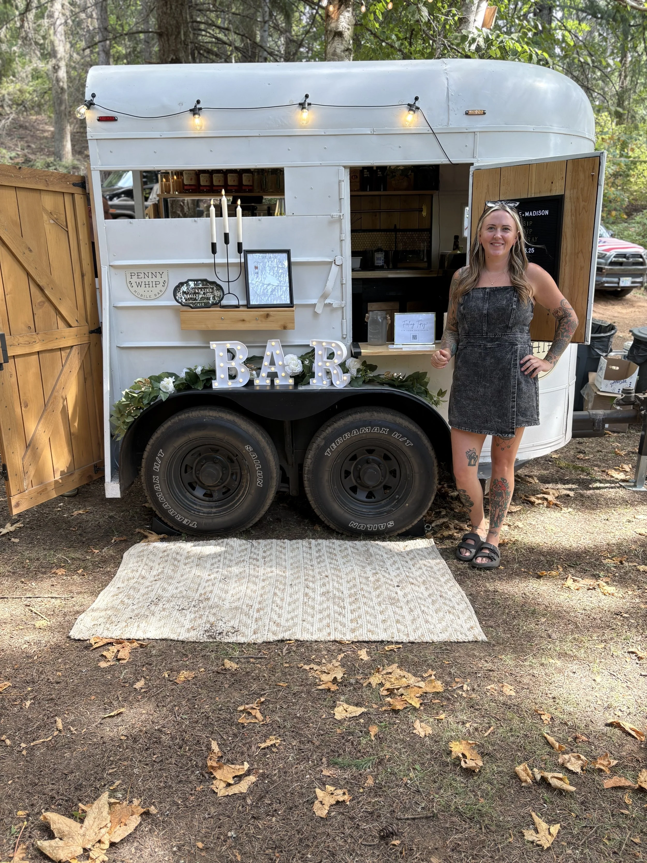Chelsie (Owner) posing at this country inspired wedding, with esthetic rug and beautiful decor, large bar sign