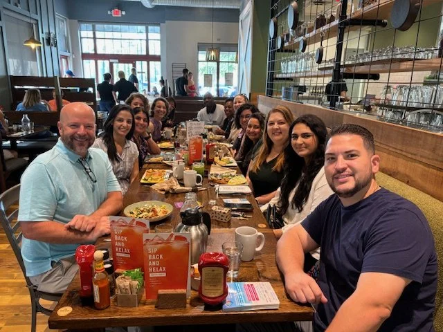 Group of people sitting around a table in a restaurant, smiling and enjoying a meal together.