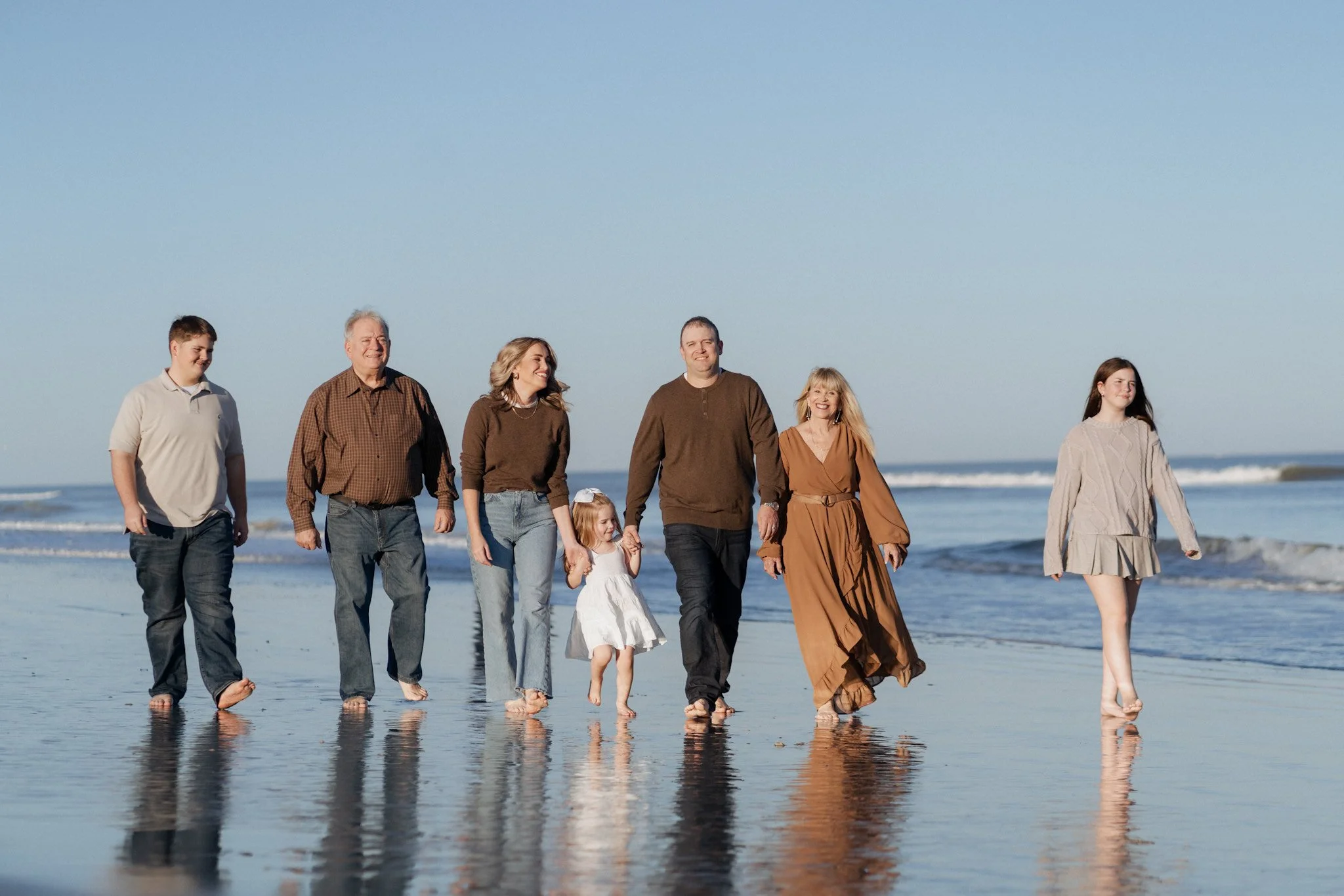 An extended family walks on the beach in Amelia Island near the Ritz Carlton. You can see their reflection in the water.