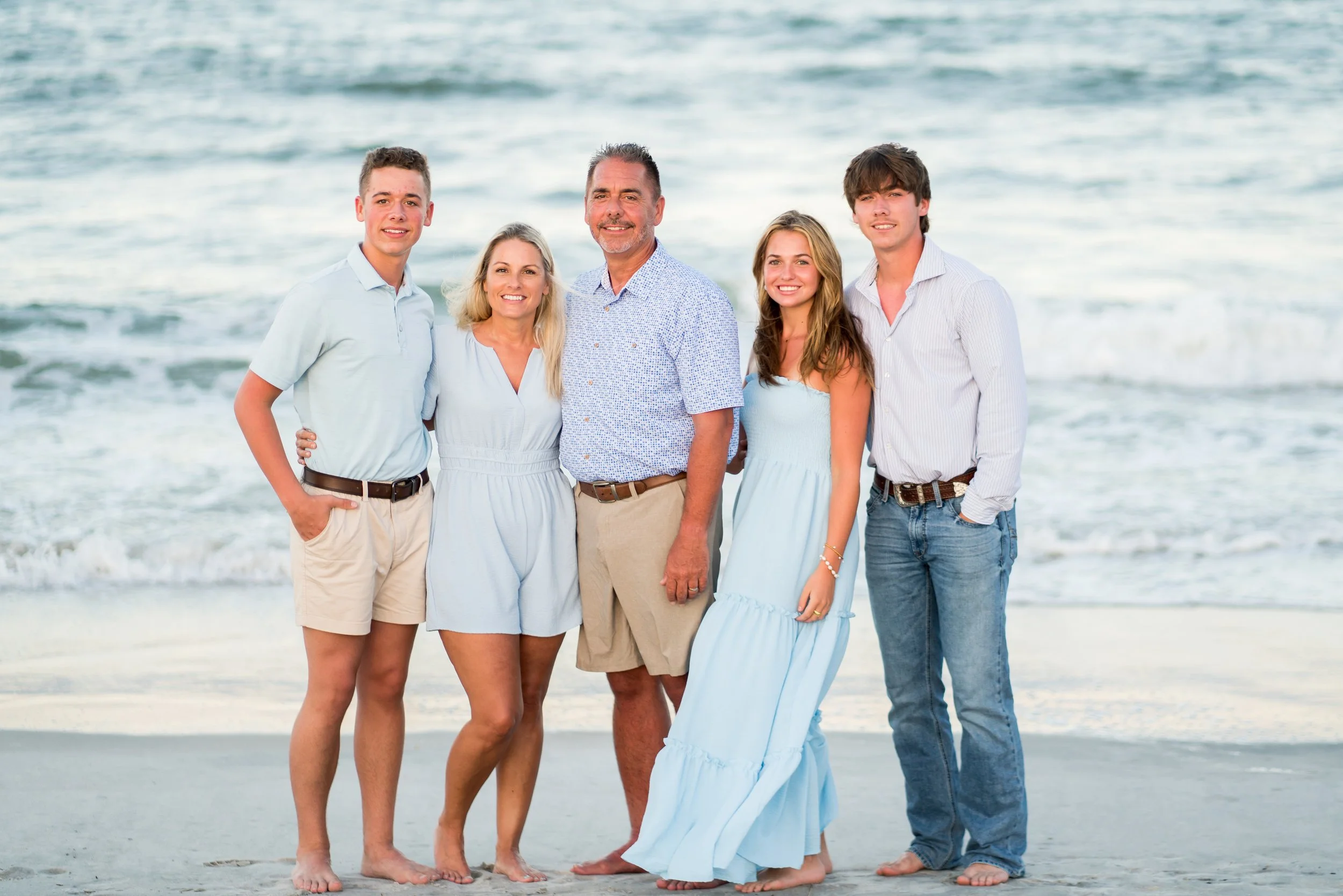 A family vacationing on Amelia Island poses in front of blue water at The Omni Resort on Amelia Island.