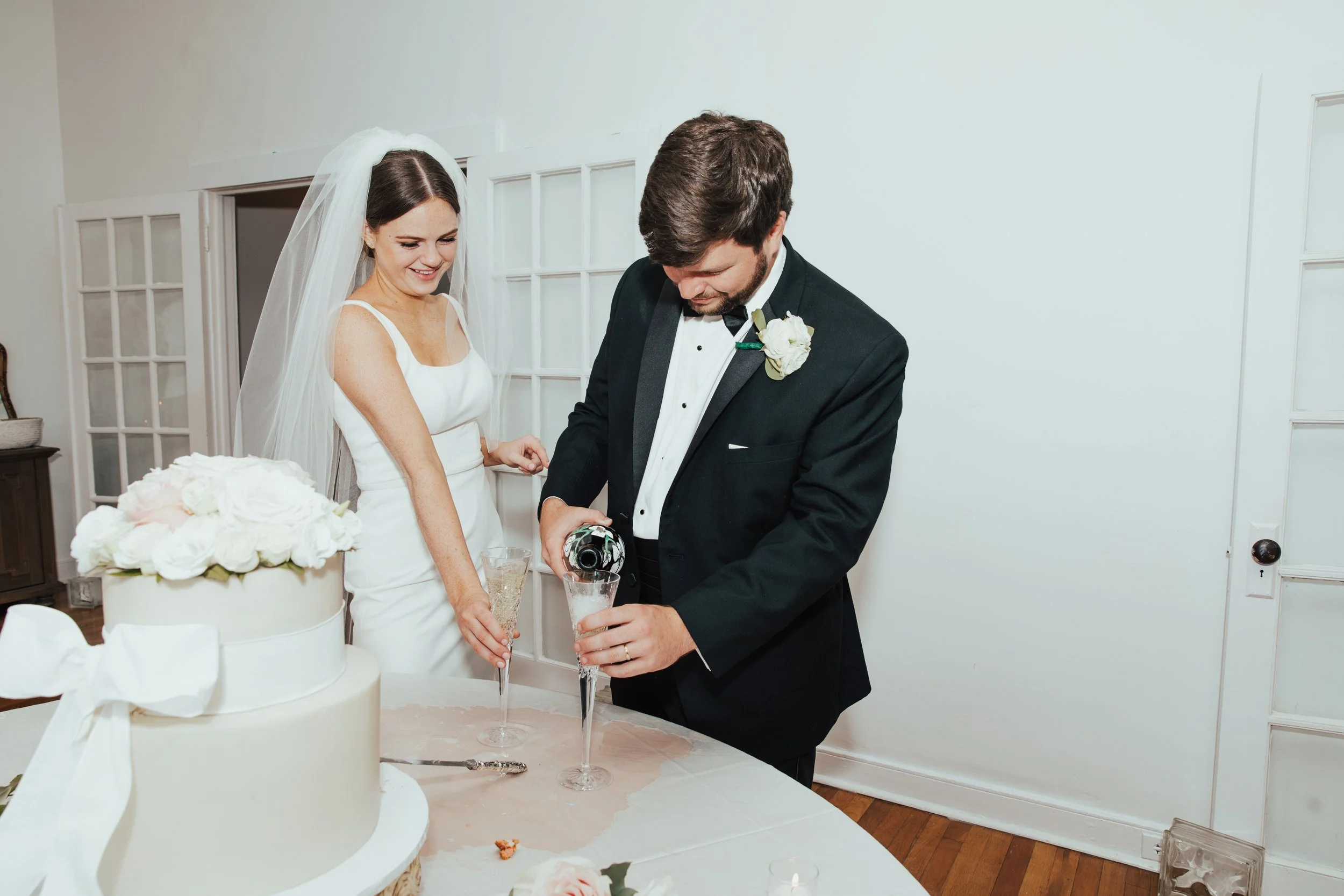 Bride and groom celebrate by pouring champagne into glasses at their wedding reception.
