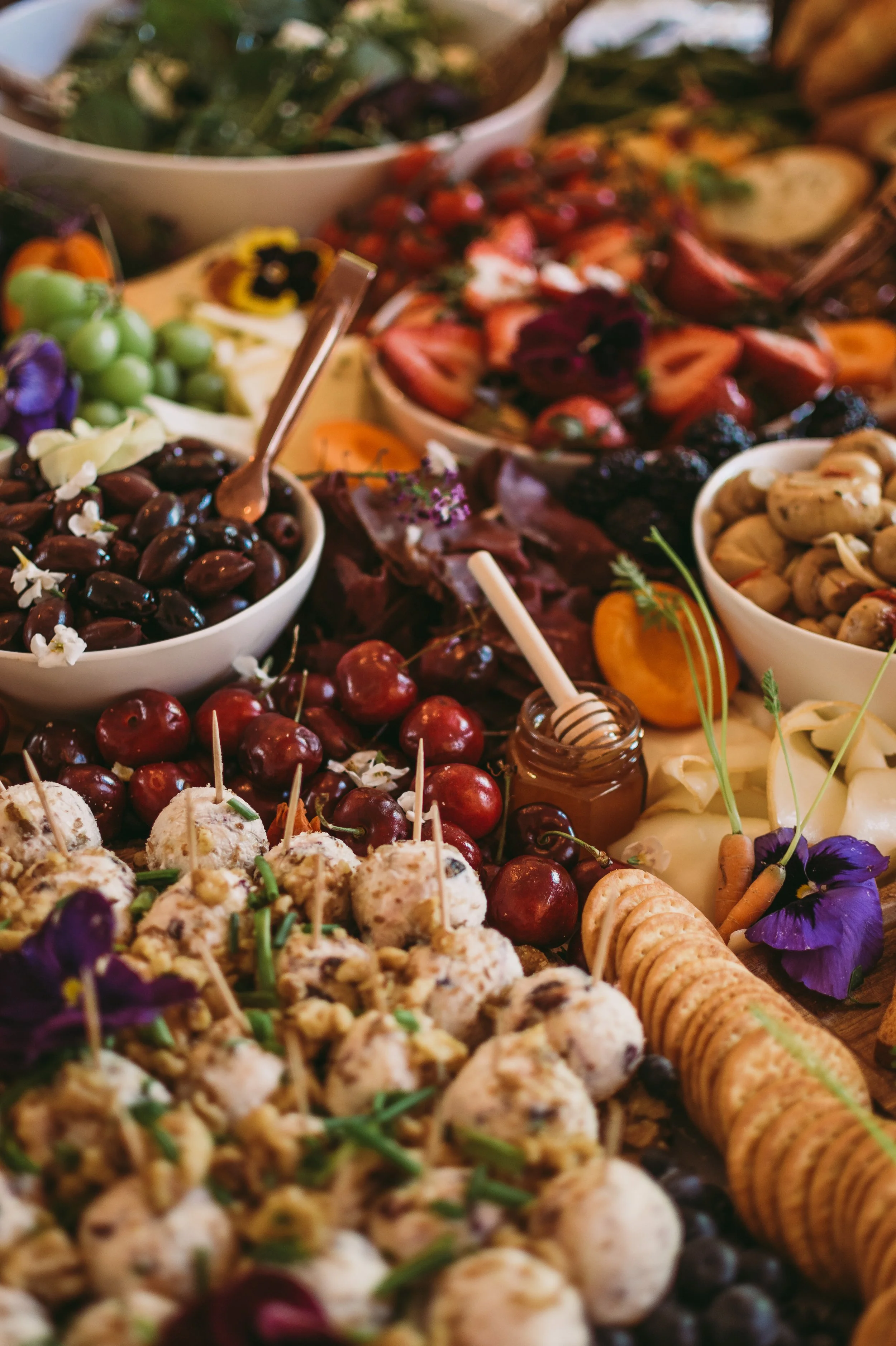 A variety of bowls with different types of cheeses, grapes, strawberries, and crackers arranged on a table, with some flowers and honey.