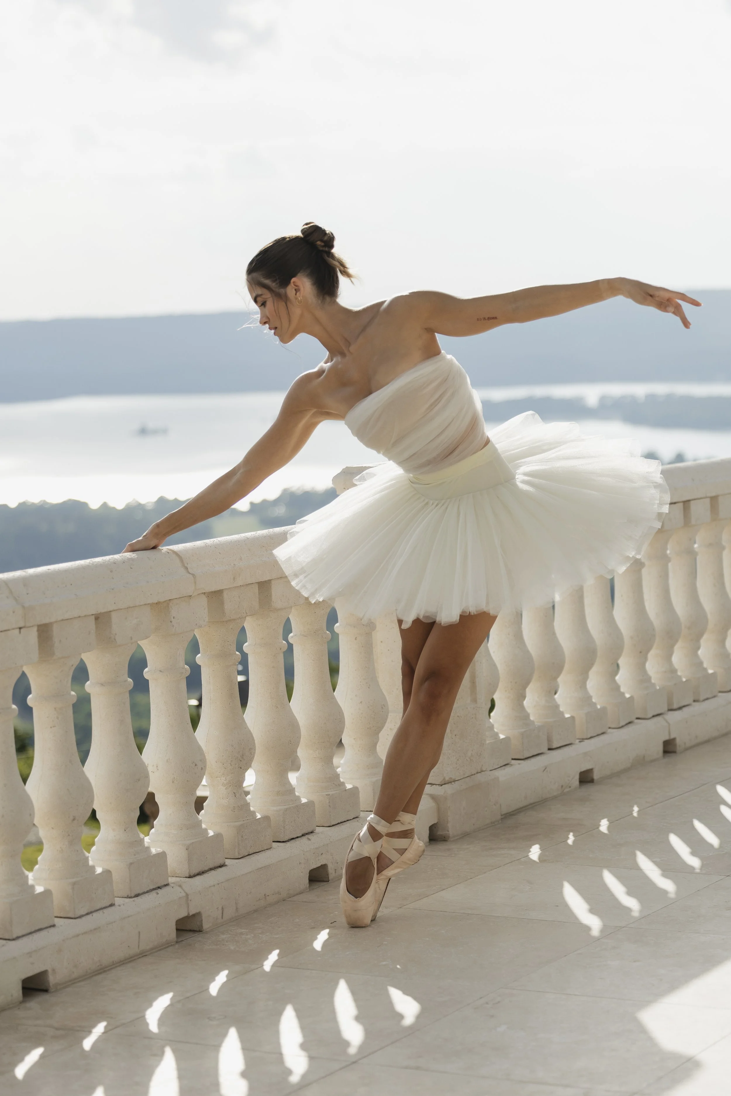 Bride in white tulle ballet gown striking a graceful ballerina pose en pointe at stone balustrade overlooking Alabama mountains and lake, bridal editorial at Stone Haven Weddings by Erin Daniel, middle Tennessee wedding photographer