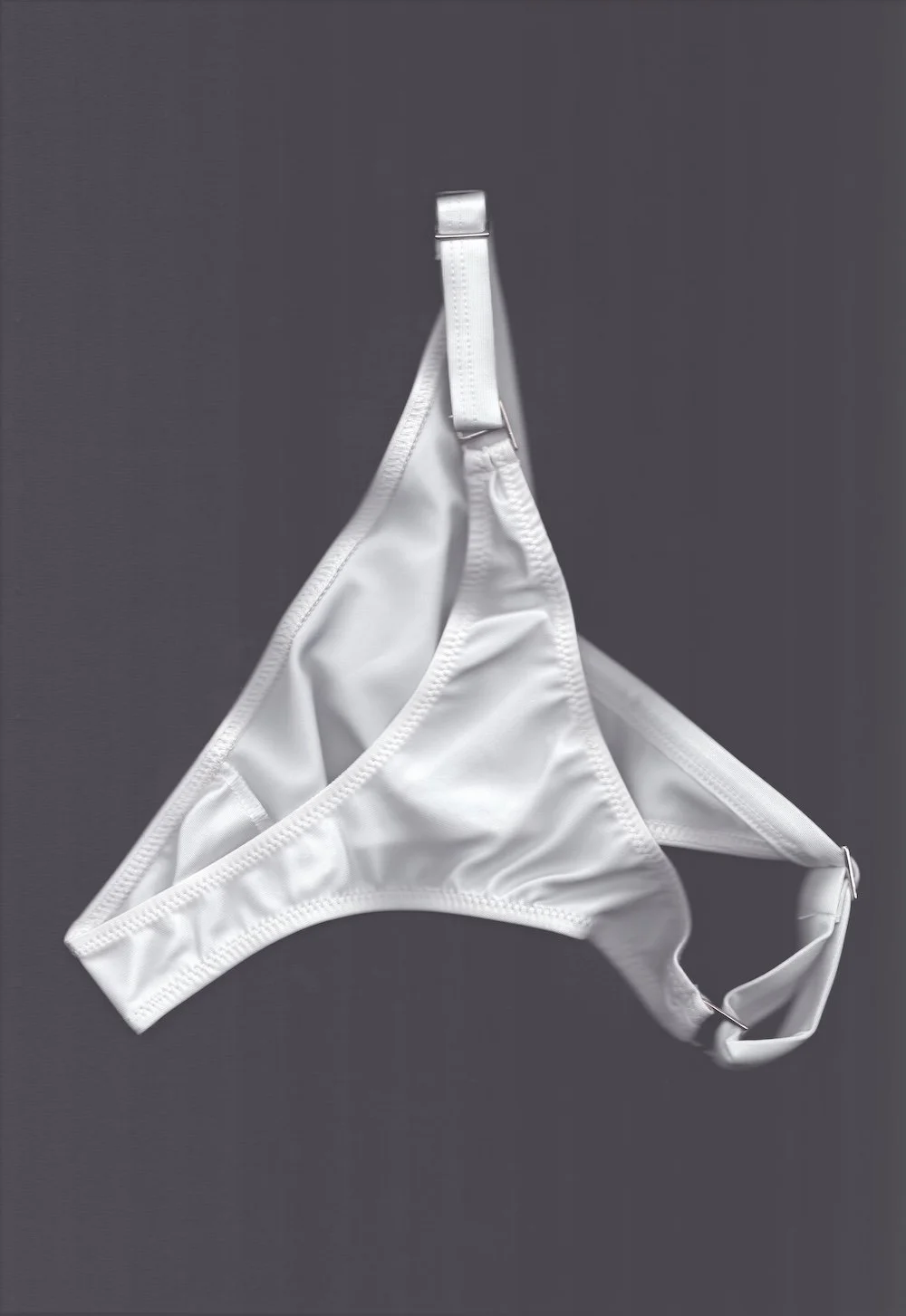 White lingerie brief with adjustable side fastenings, photographed flat on a grey background