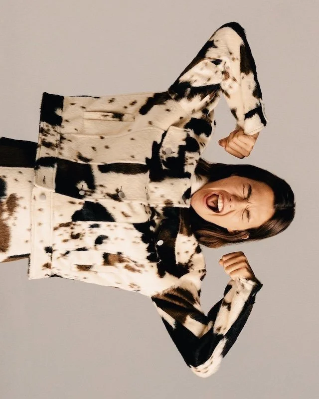 Model laughing mid-movement in a bleached monochrome print jacket and matching trousers, image inverted