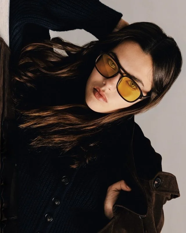 Yellow tinted sunglasses and long dark hair, worn with a black corduroy jacket over brown suede