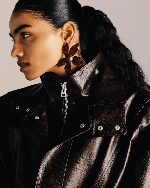 Close crop of a dark brown leather biker jacket zipped to the chin, worn with an oversized carved floral earring