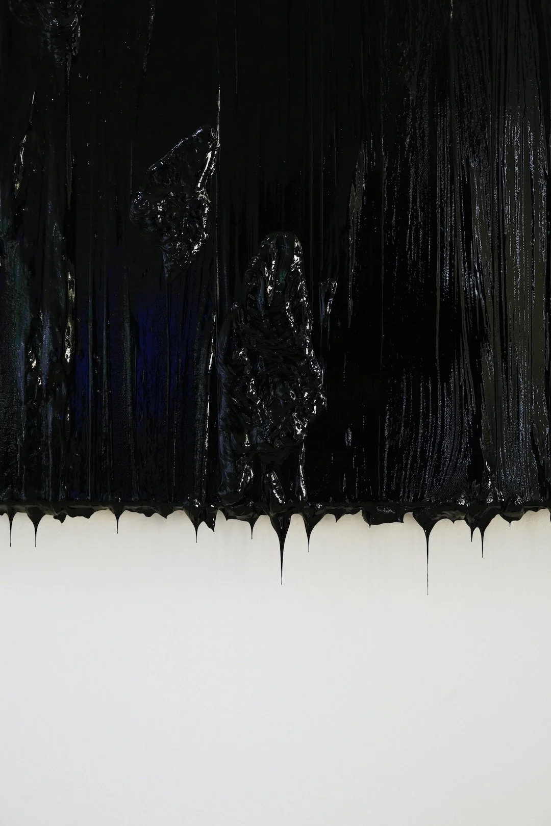 Close crop of a black textured painting with glossy drips running down the surface