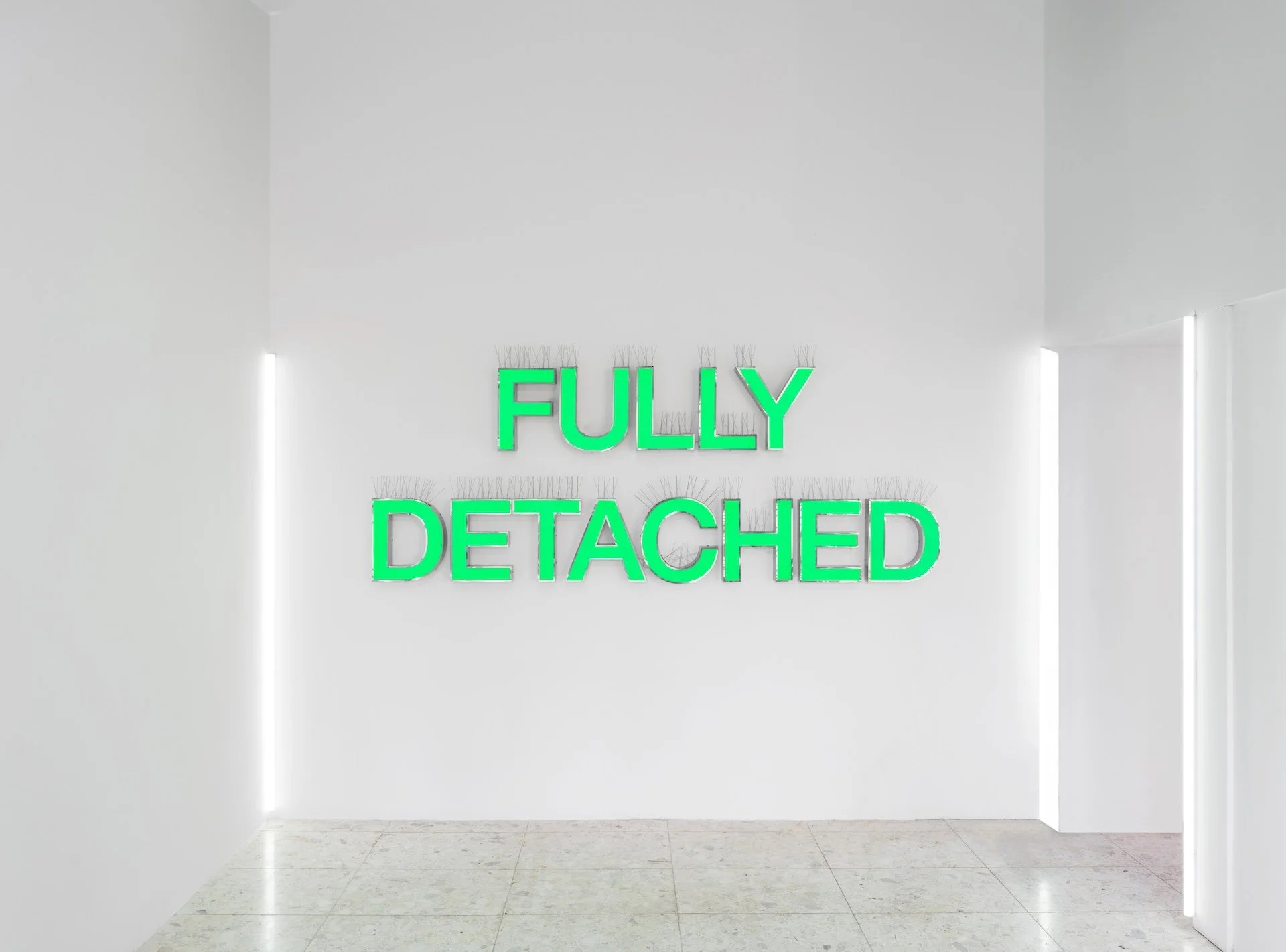 Green neon lettering reading Fully Detached mounted on a white gallery wall