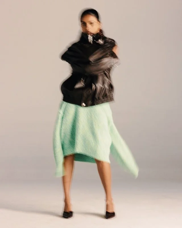 Black leather jacket over a mint green knit and skirt, captured in motion blur
