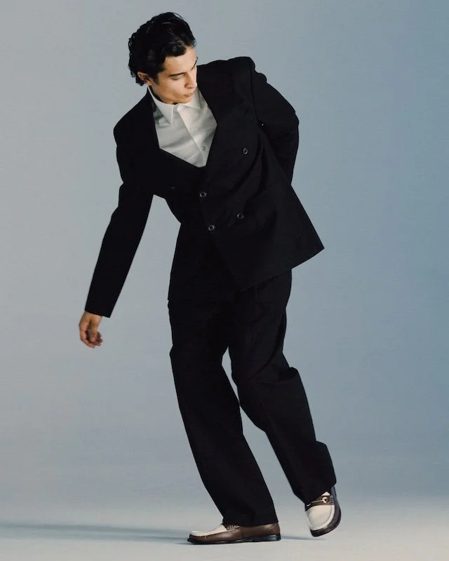 Black double-breasted suit and white shirt caught mid-stride, jacket open and swinging