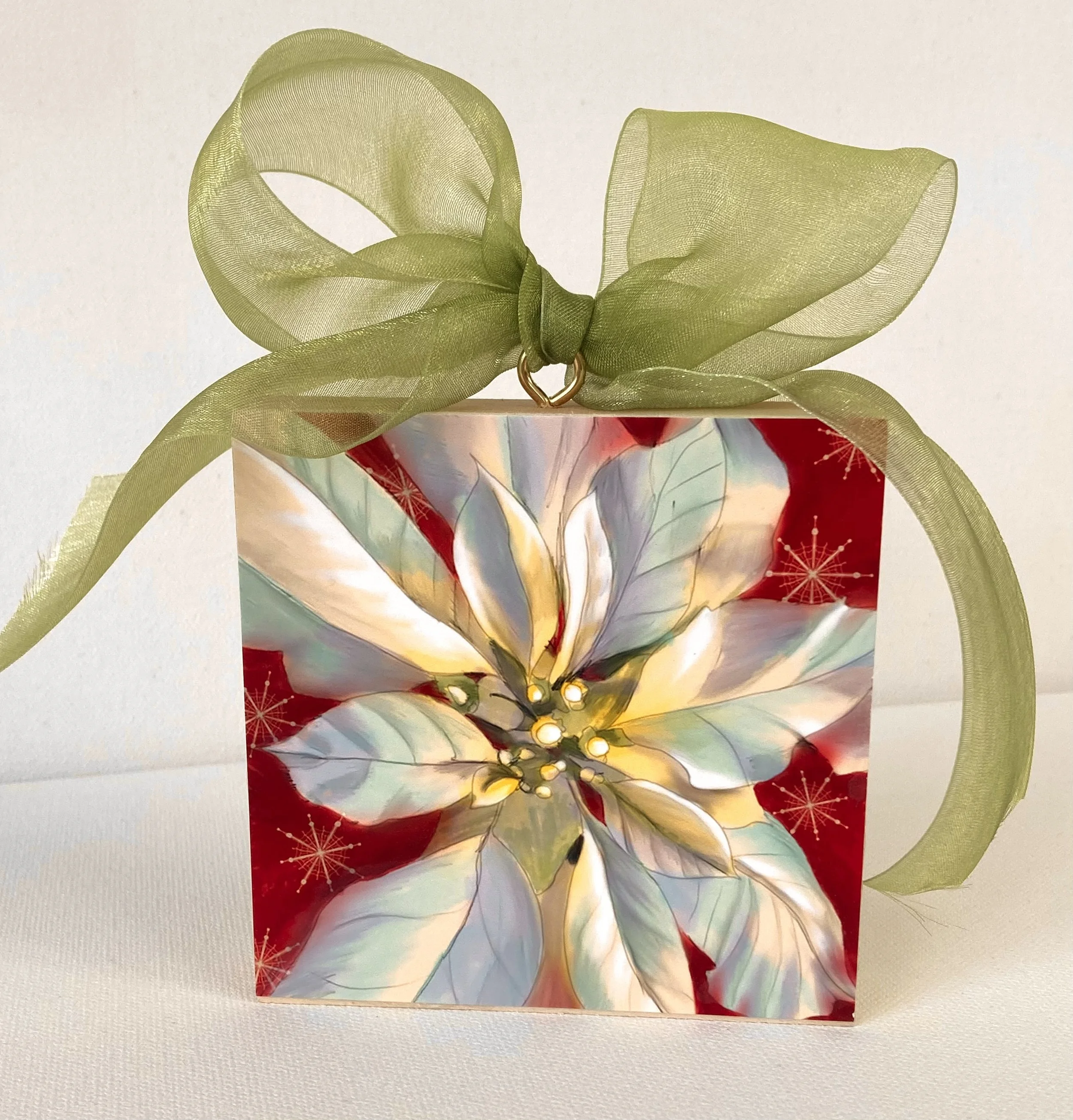 A Christmas ornament with a poinsettia design, topped with a green sheer ribbon bow.