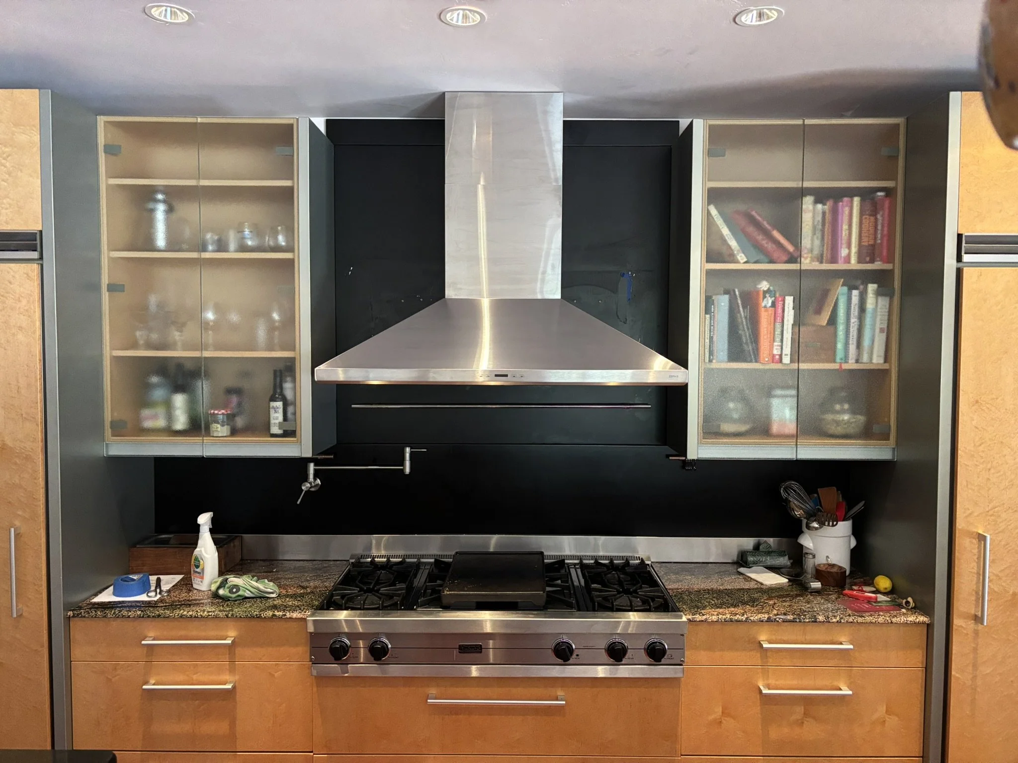 Large stainless steel vent hood installed over a gas cooktop with dark tile behind it