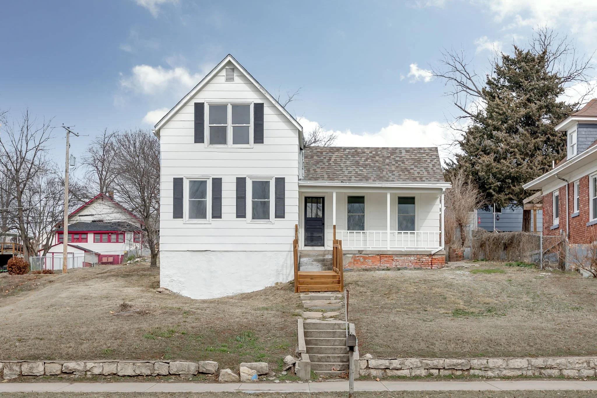 White two-story house with black shutters, front porch, and brown steps on a grassy lawn.