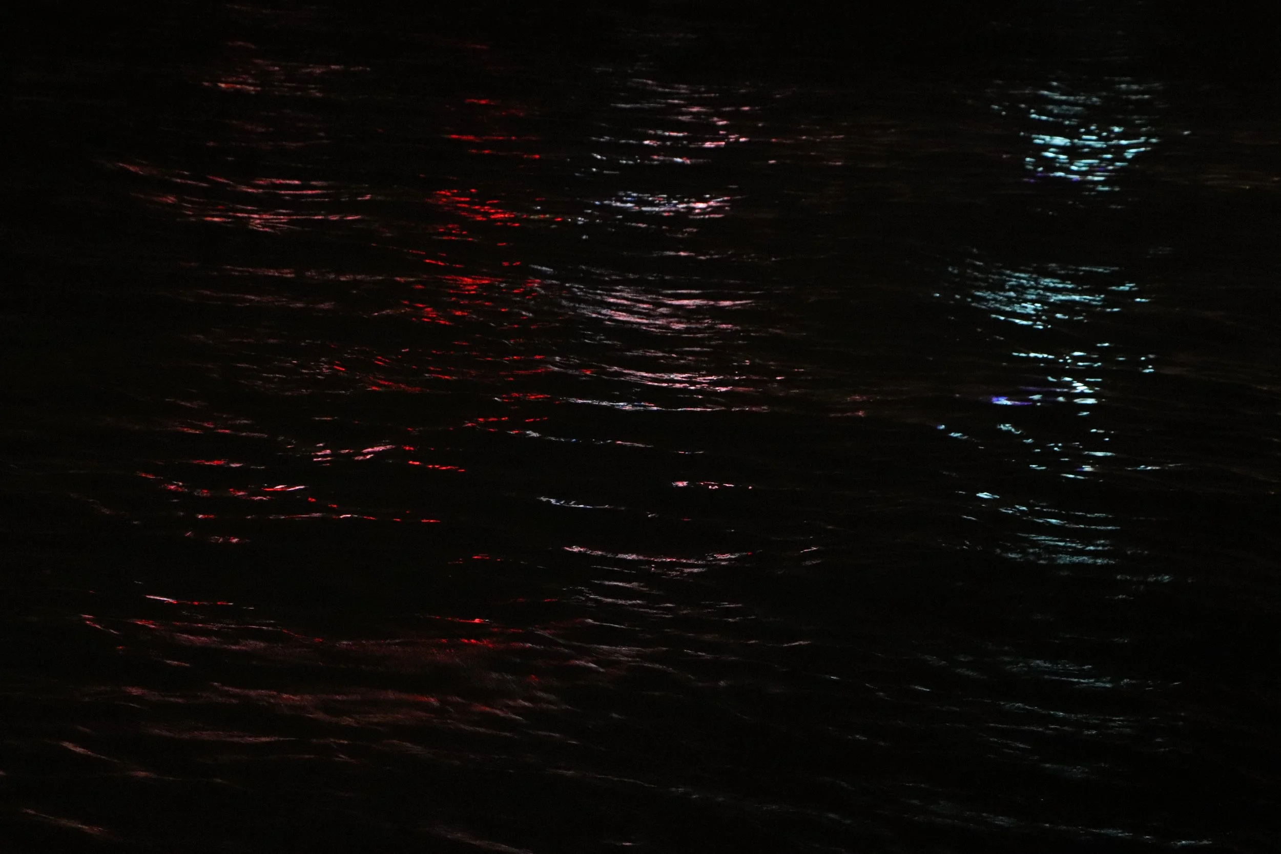 Reflections of colorful lights on dark water at night.