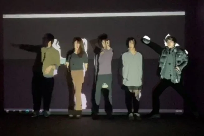 Five individuals standing in front of a dark background with some drawings or projections, posing for a photo.