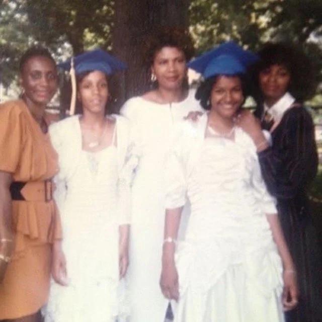 Group of women in formal attire posed together at what appears to be a graduation or celebratory occasion.