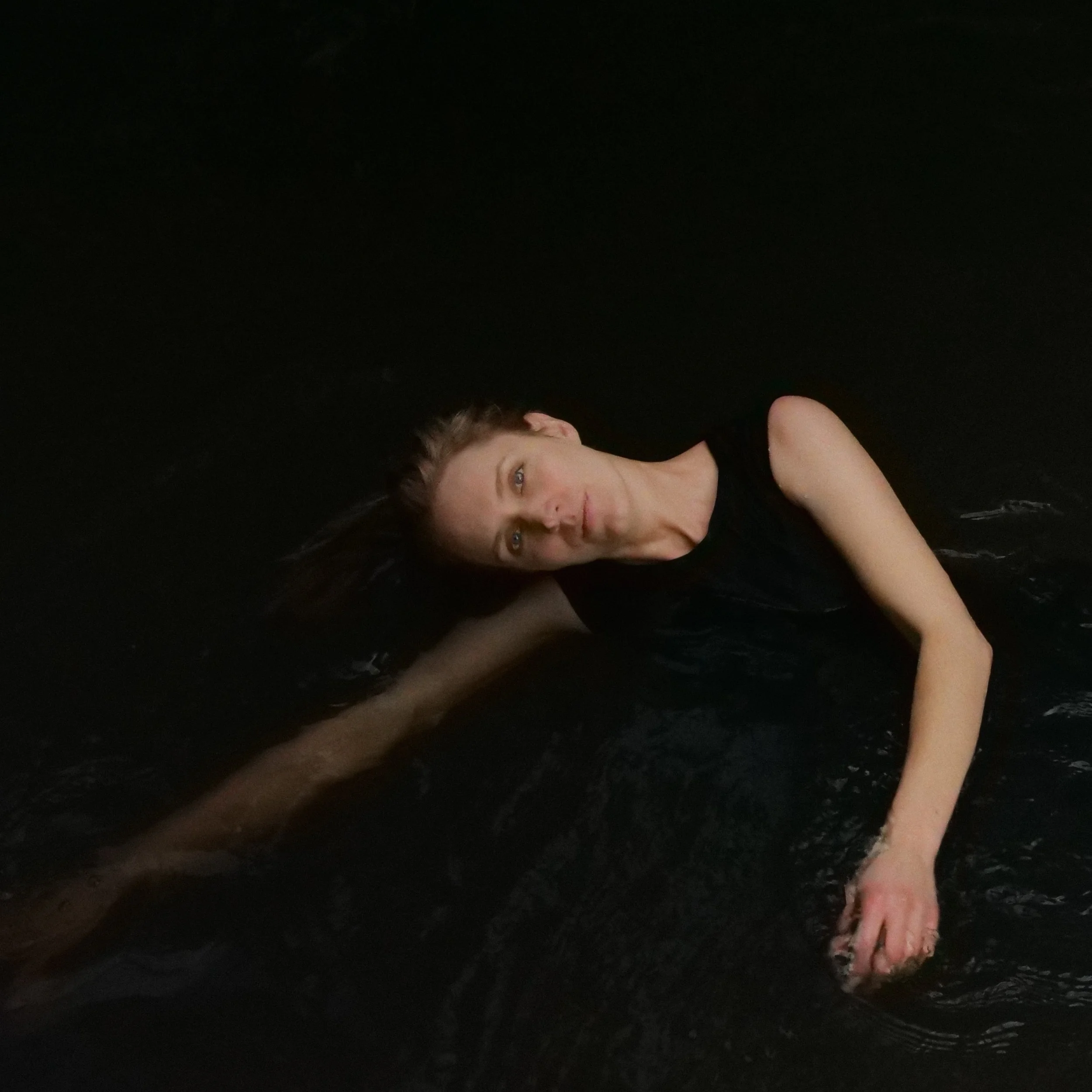 Woman in black dress floating sideways in dark water
