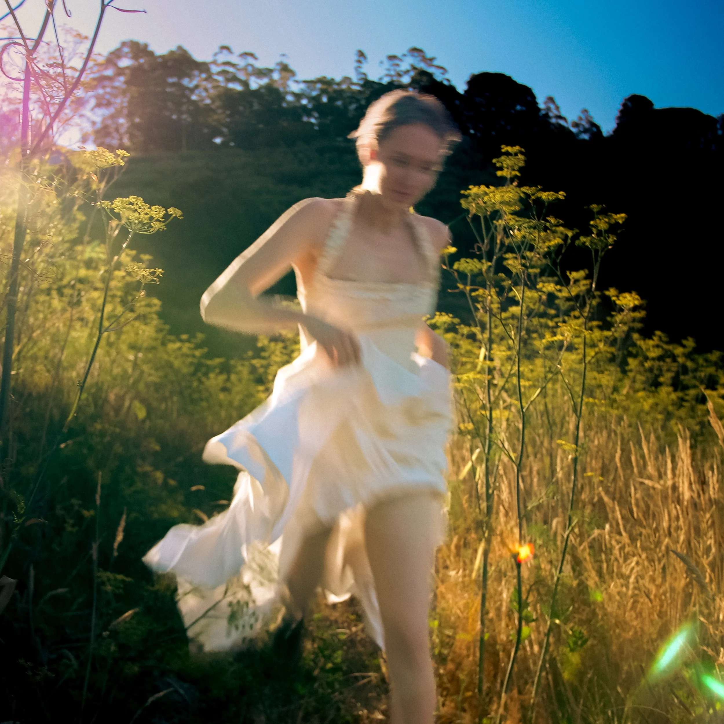 Woman in white dress running through yellow flowers in sunshine