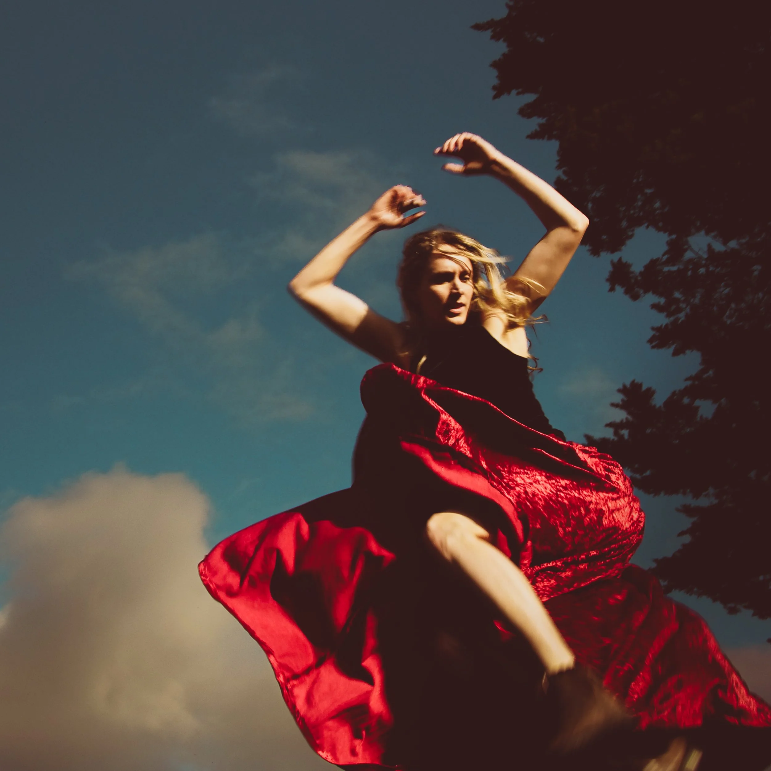 Woman in red dress leaping in the air with blue sky and white clouds
