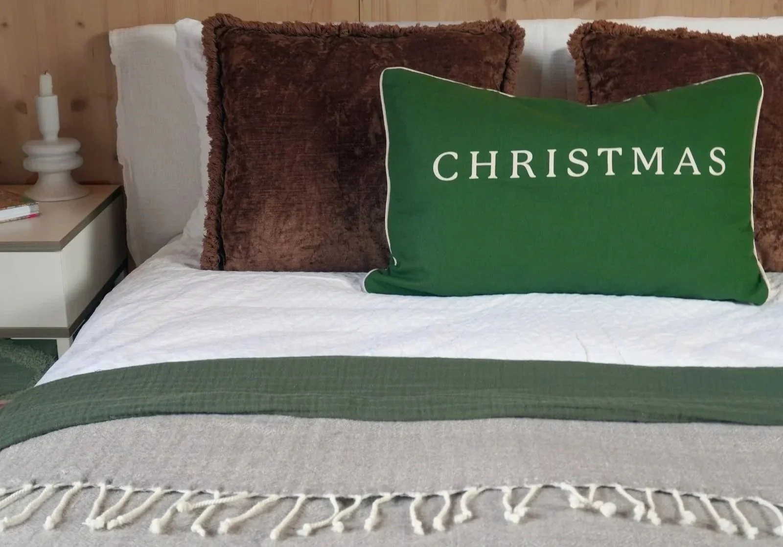Bedroom decorated in white, mocha, and green Christmas accents with soft textiles and seasonal greenery.