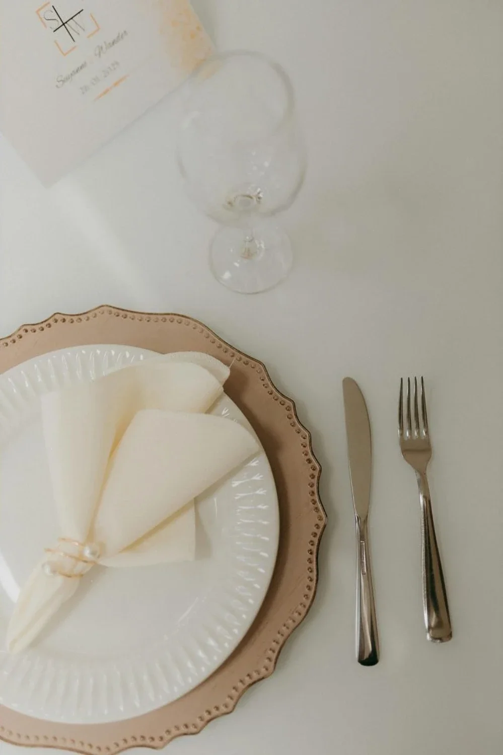 A minimalist interior table setting for one featuring a ceramic plate and metallic cutlery arranged on the right side of a natural wood dining table.