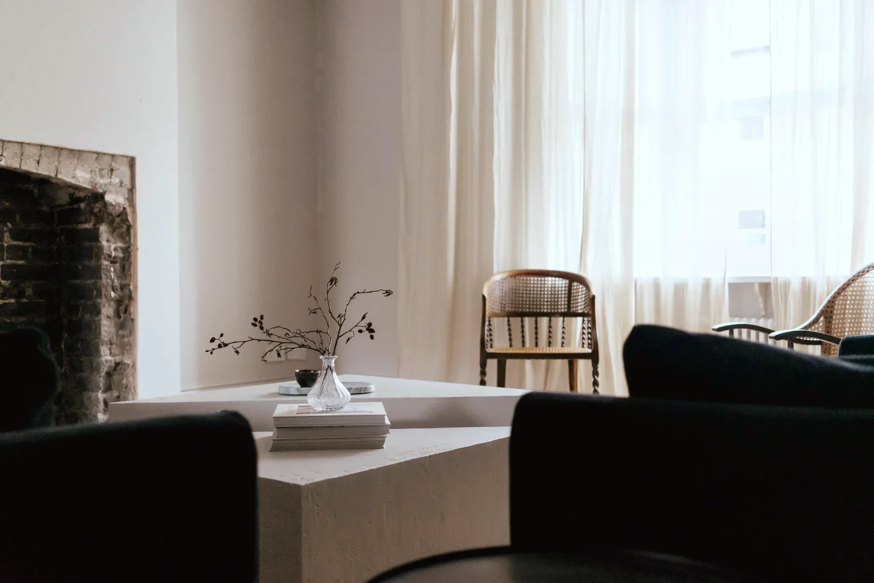 Moody living room interior with dramatic sunlight filtering through multi-pane windows, creating rhythmic shadows and a nest-like sense of comfort.