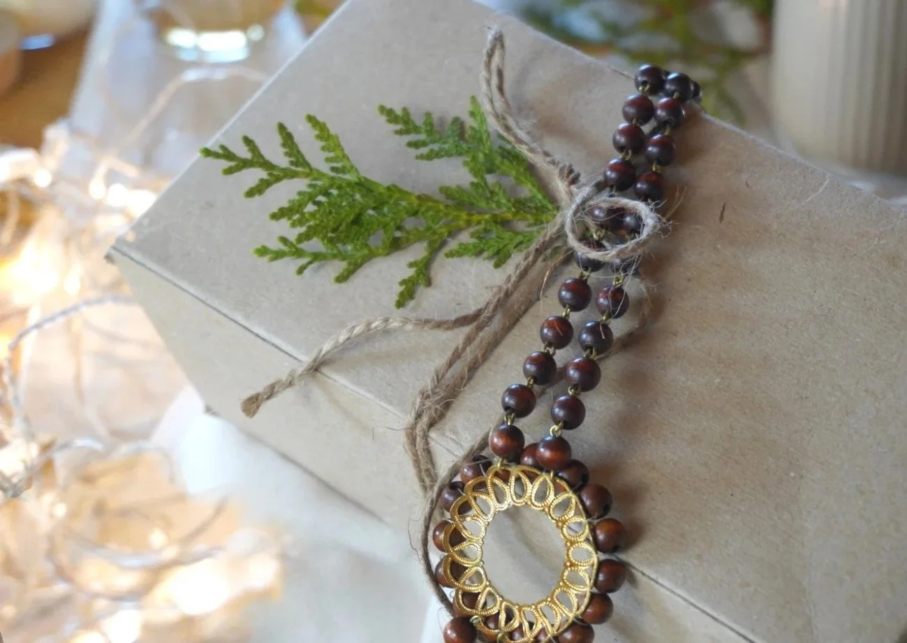 Christmas gift wrapped in brown paper with natural twine, wooden beads, and pine sprigs for eco-friendly festive wrapping inspiration.