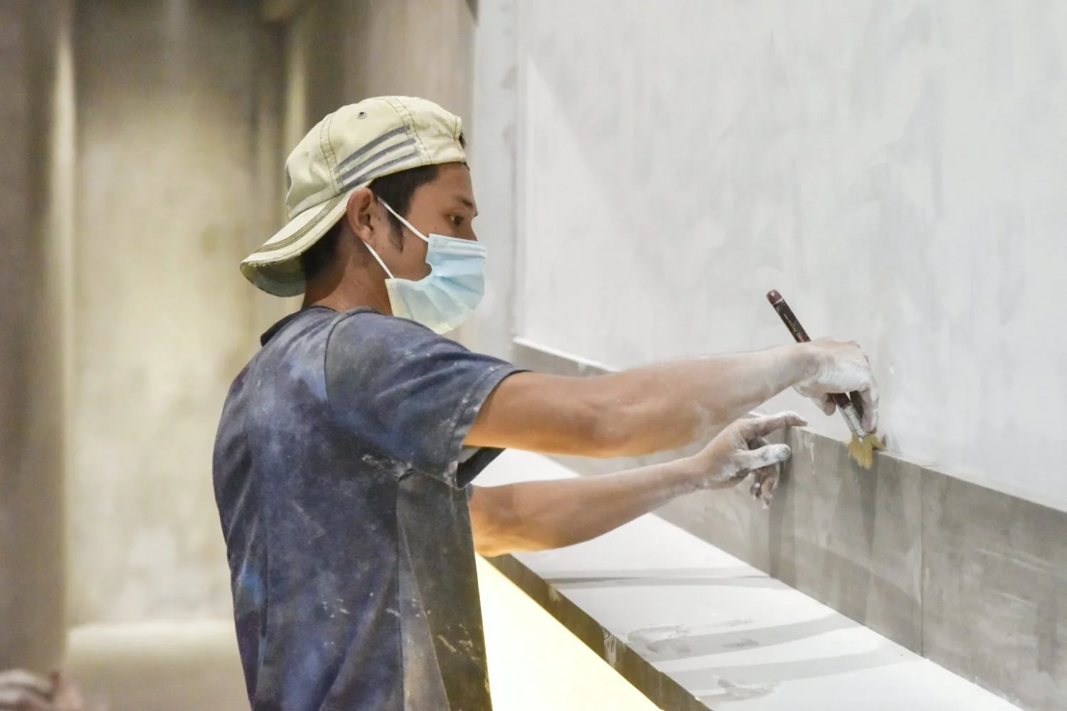 Craftsman applying microcement around bathroom edges with a brush during installation.