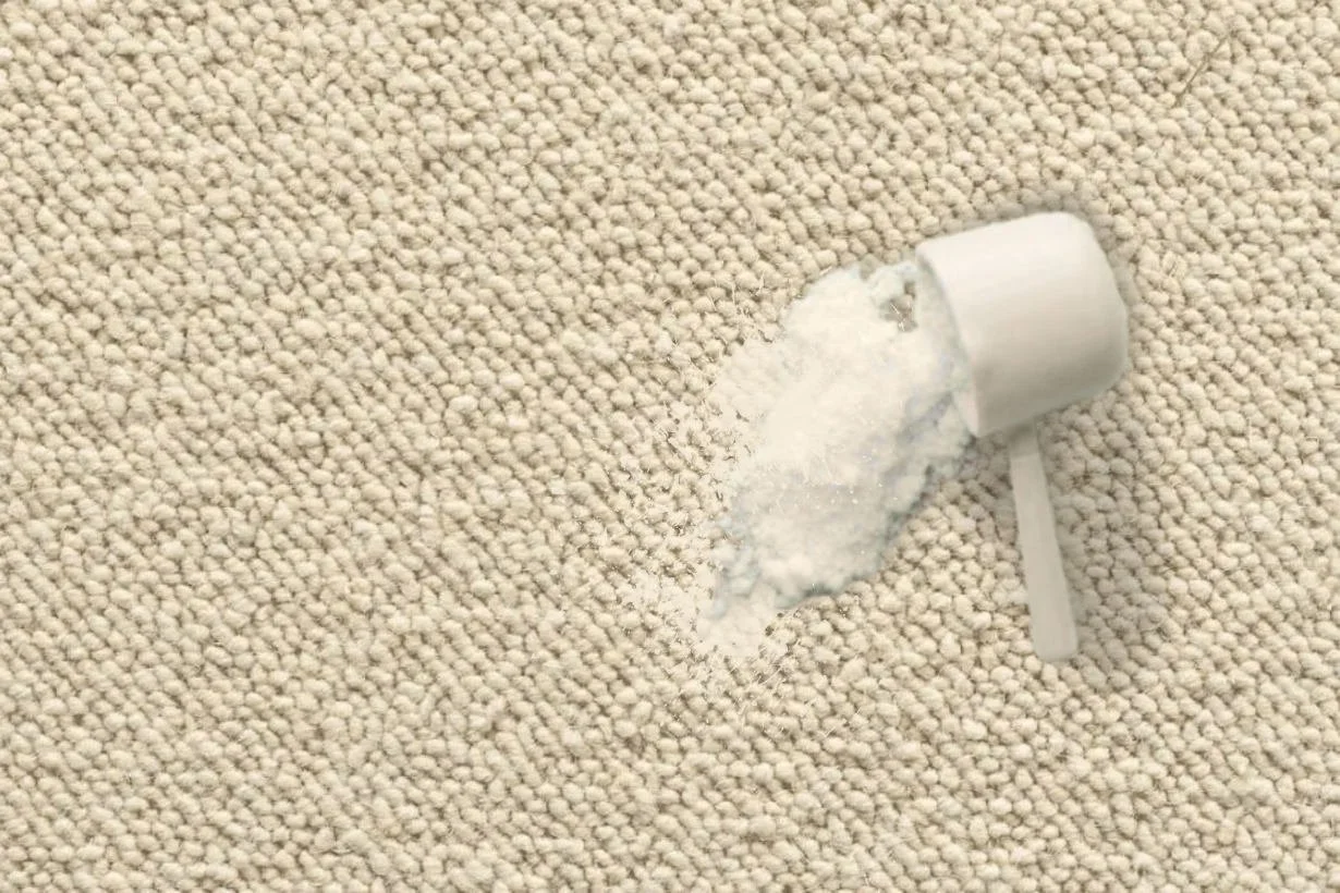 Overhead bird's-eye view of a beige berber wool carpet with a powdery spill, multi-tonal yarn designed for durability and concealing everyday wear.