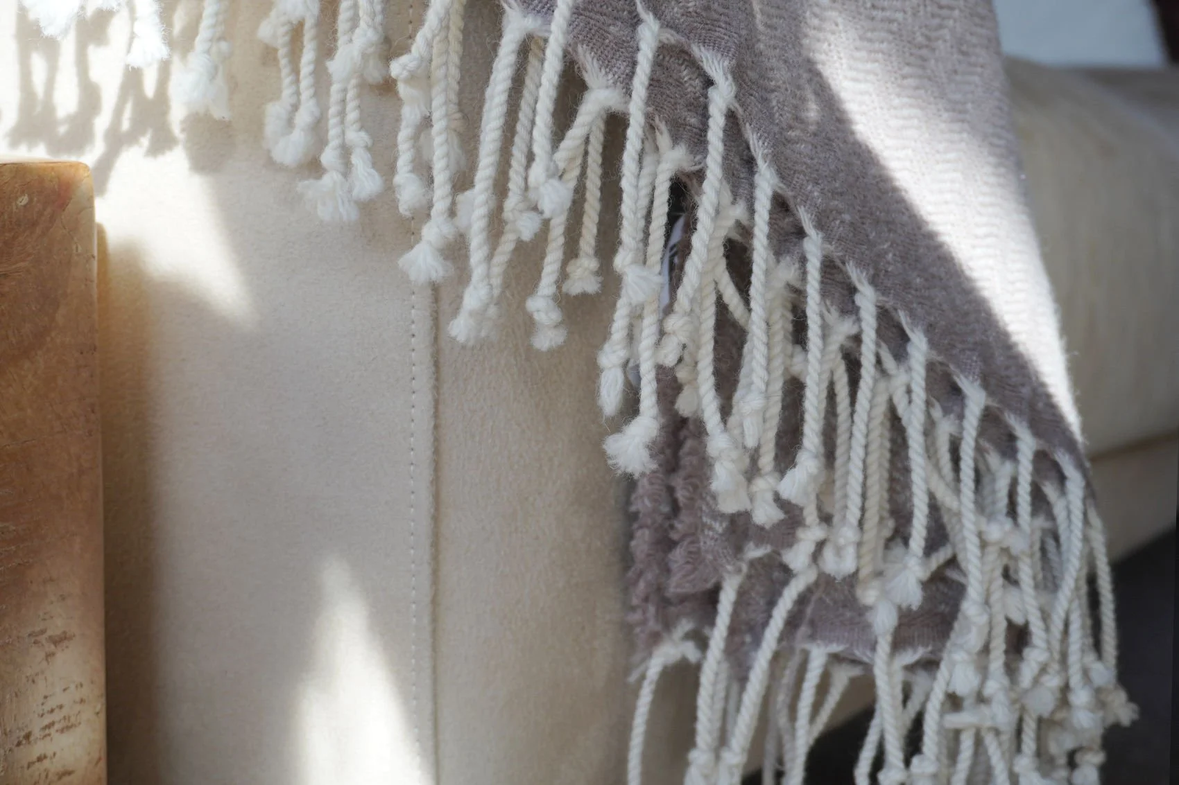 Close-up of a fringed wool blanket draped over a beige sofa, lit by natural sunlight, highlighting soft textures.