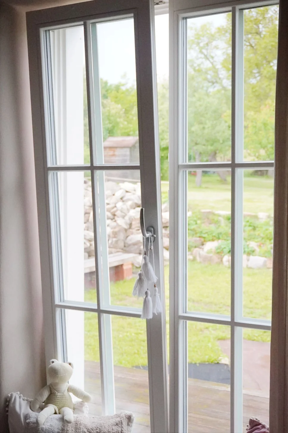 A tall interior French window opened ajar at the top, frame-view looking out onto a serene and lush green garden layout.