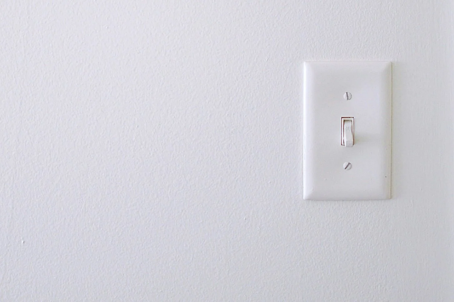 Minimalist white wall with a single light switch, representing a high-touch area to sanitize.