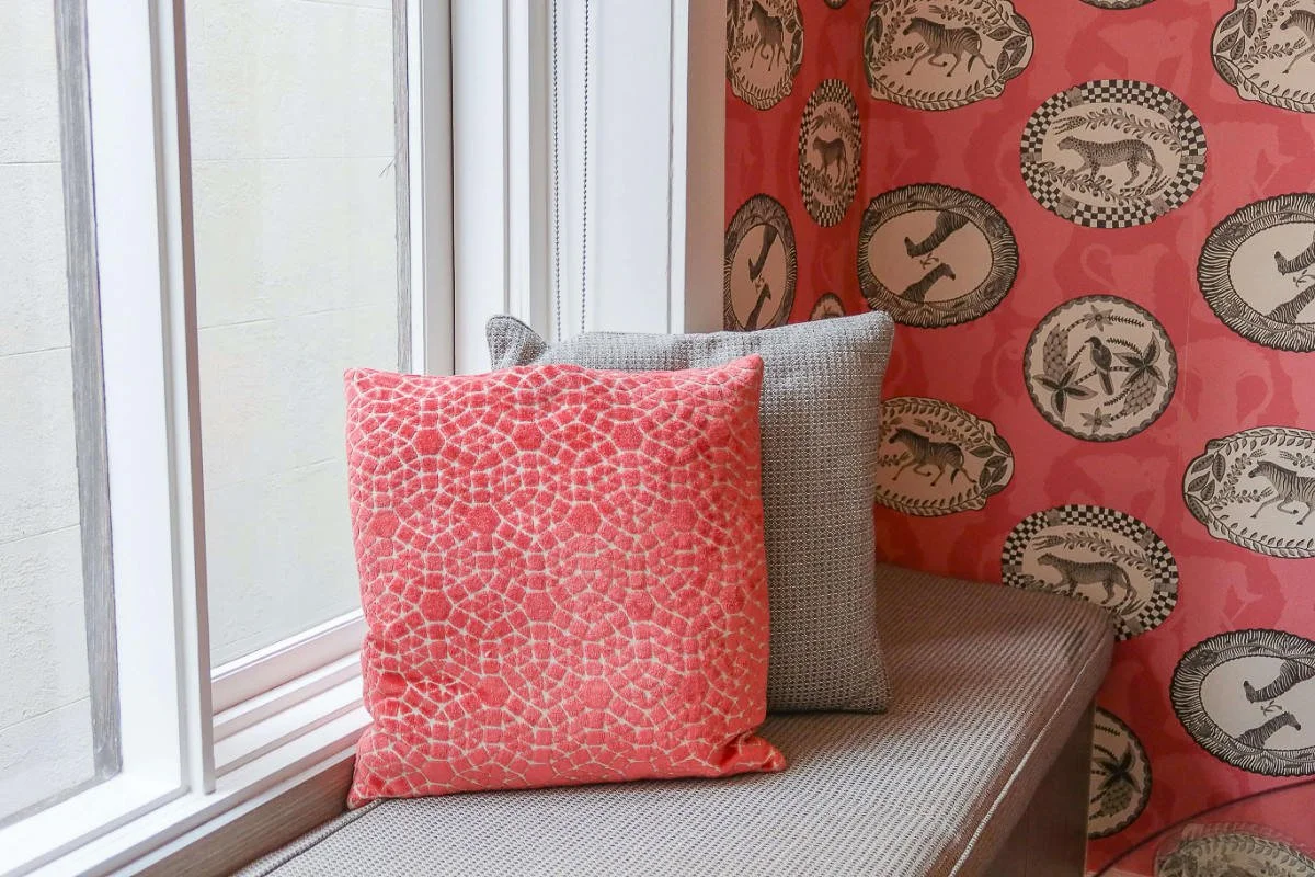 A cosy window nook with red anima themed wall-paper and soft grey and red cushions to portray selective wallpaper accents.