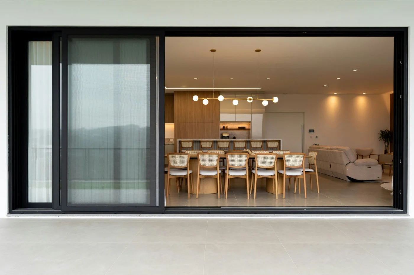 A wide perspective shot looking through a large sliding glass door into a sleek, open-plan dining room of a contemporary home.
