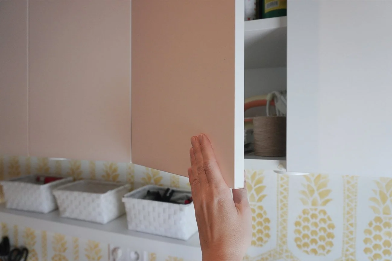 A hand opening a minimalist white upper storage cabinet, showcasing smart cabinetry design ideas for maximizing space in a compact utility room.