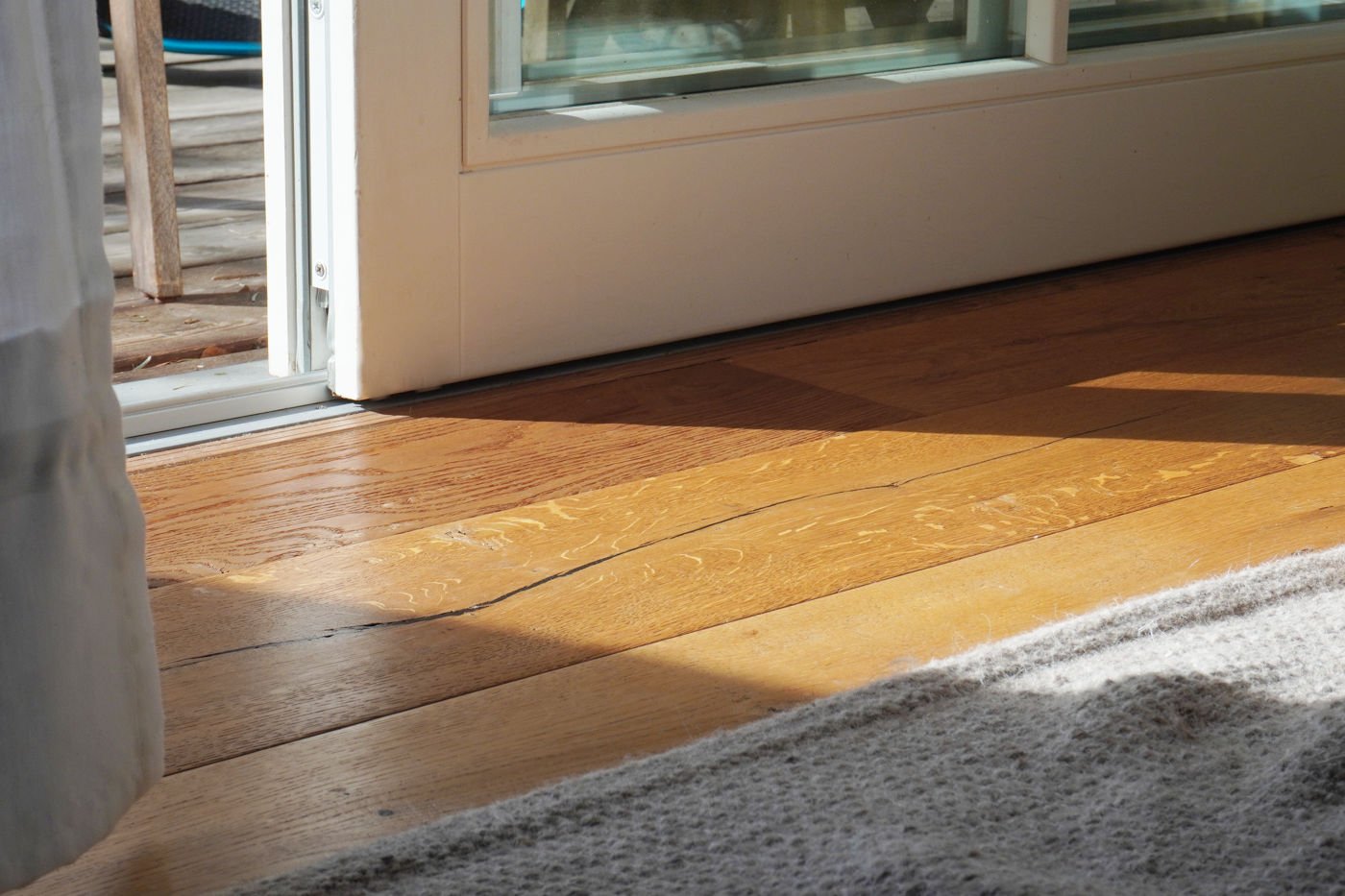 Wooden floor illuminated by sunlight near an open door leading to a terrace, emphasizing the connection between indoor and outdoor living spaces.