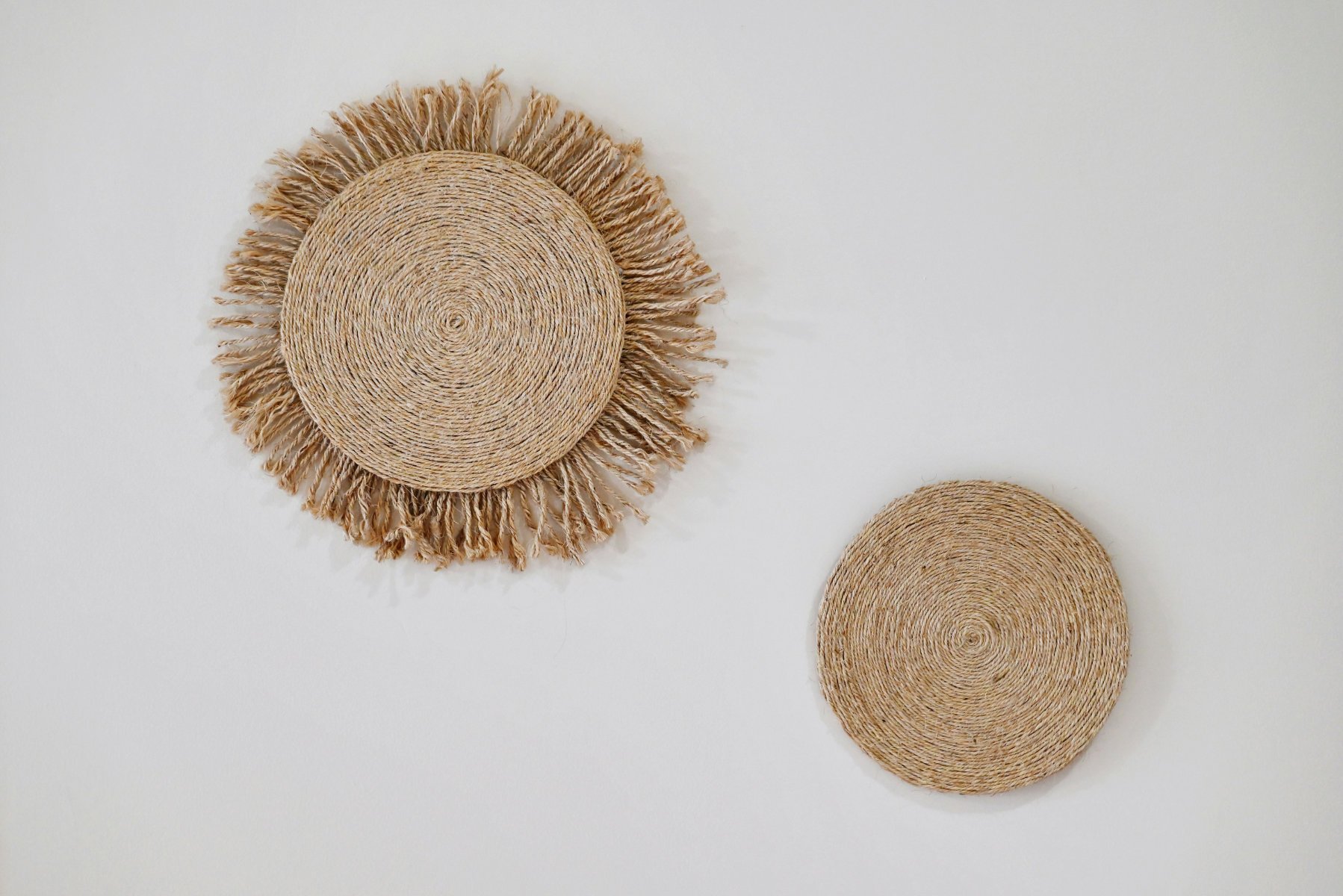 atural wall decor featuring two circular woven sea grass or banana leaf pieces on a white wall, adding texture and organic warmth to a minimalist interior.