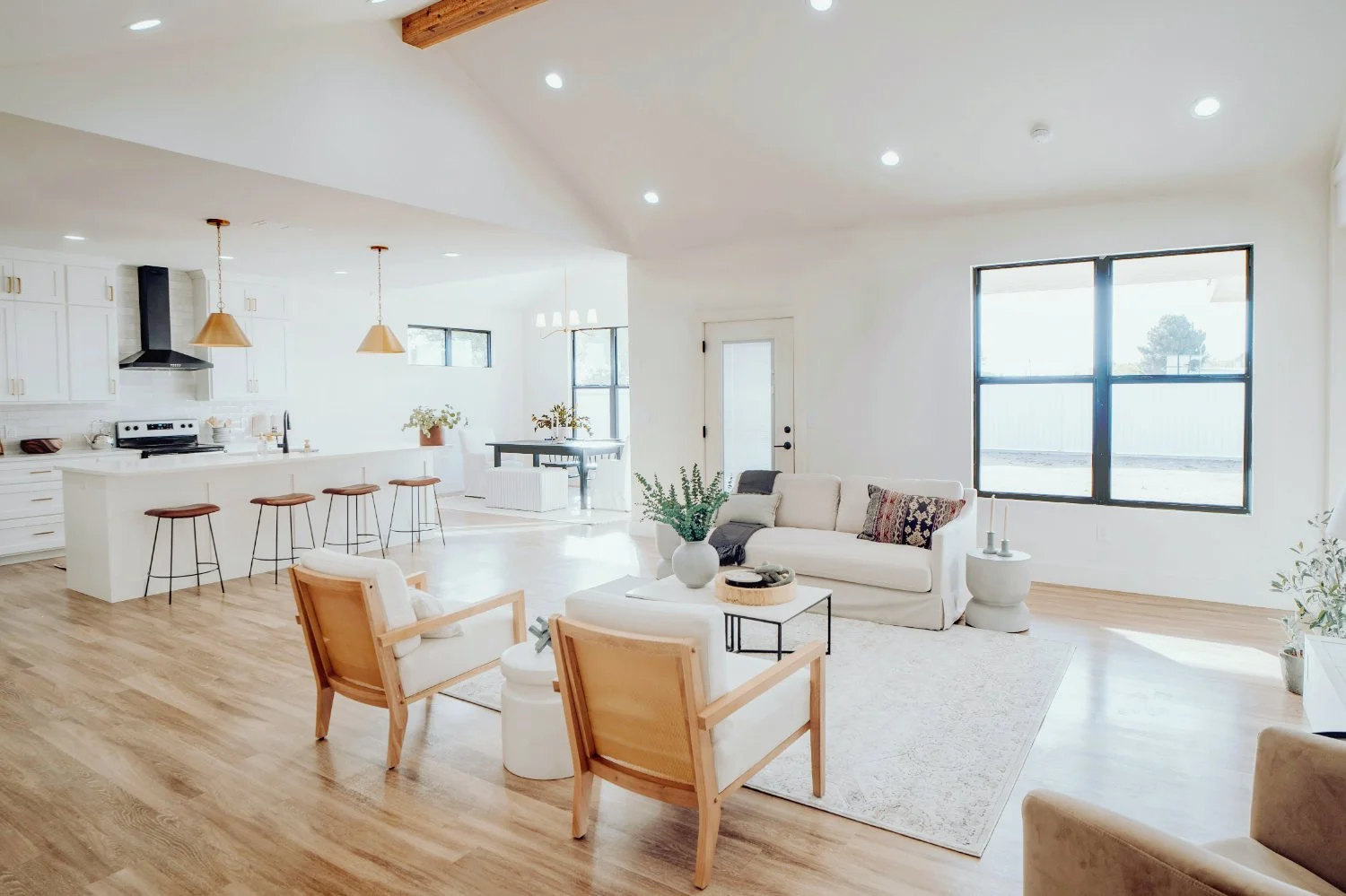 A bright and spacious open-plan kitchen and living room featuring large windows with sleek black frames and minimalist metal details.
