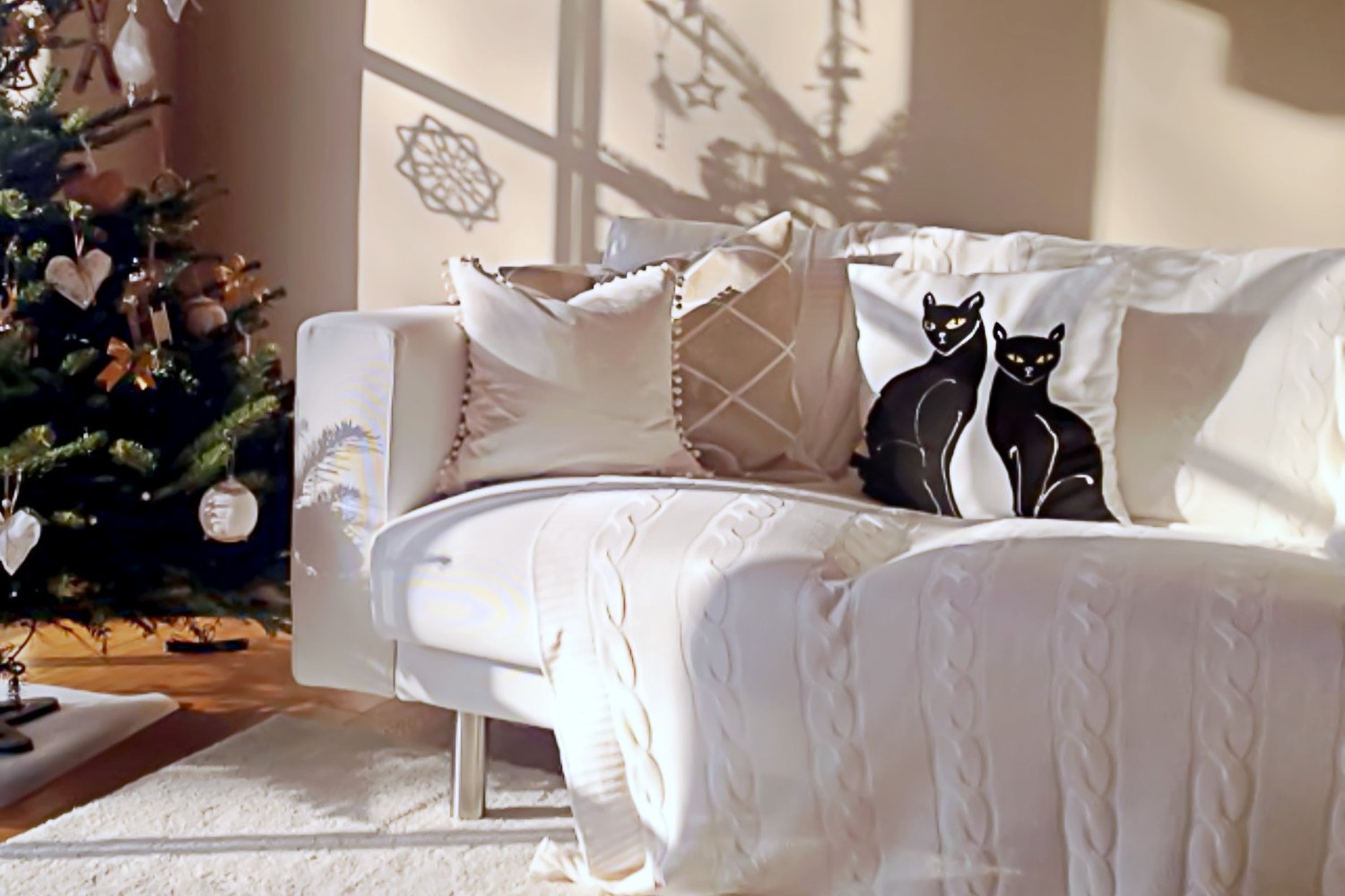 White inviting living room with knitted blanket and cushions in muted colours picturing two black cats portraying holistic interior.