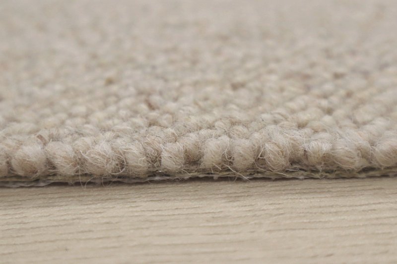 Macro photography of a level loop wool carpet weave, showing the architectural detail and porous structure of natural sustainable flooring.