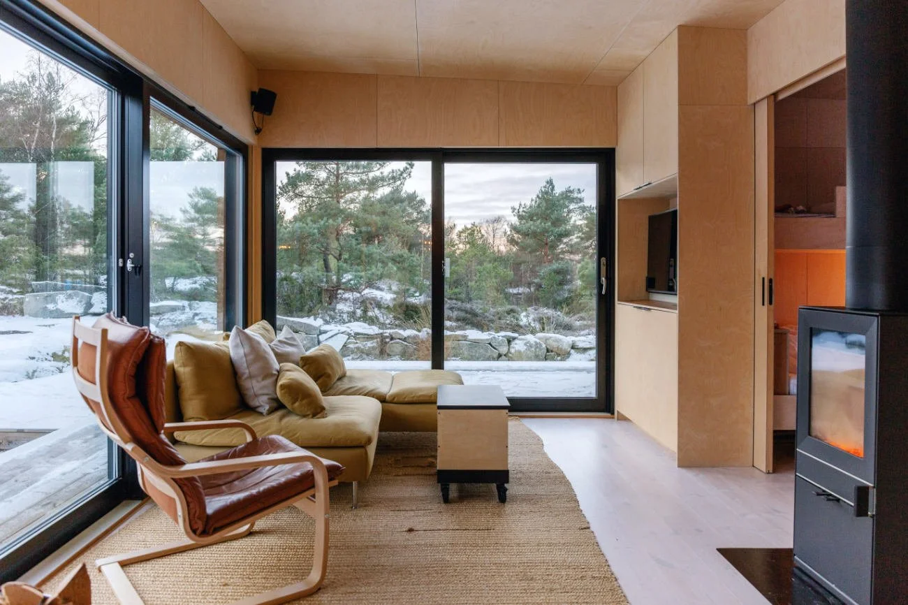 A large open-plan living room with wood cladding, a fireplace, and vast floor-to-ceiling windows, illustrating how unshielded glass can cause stress after dusk.