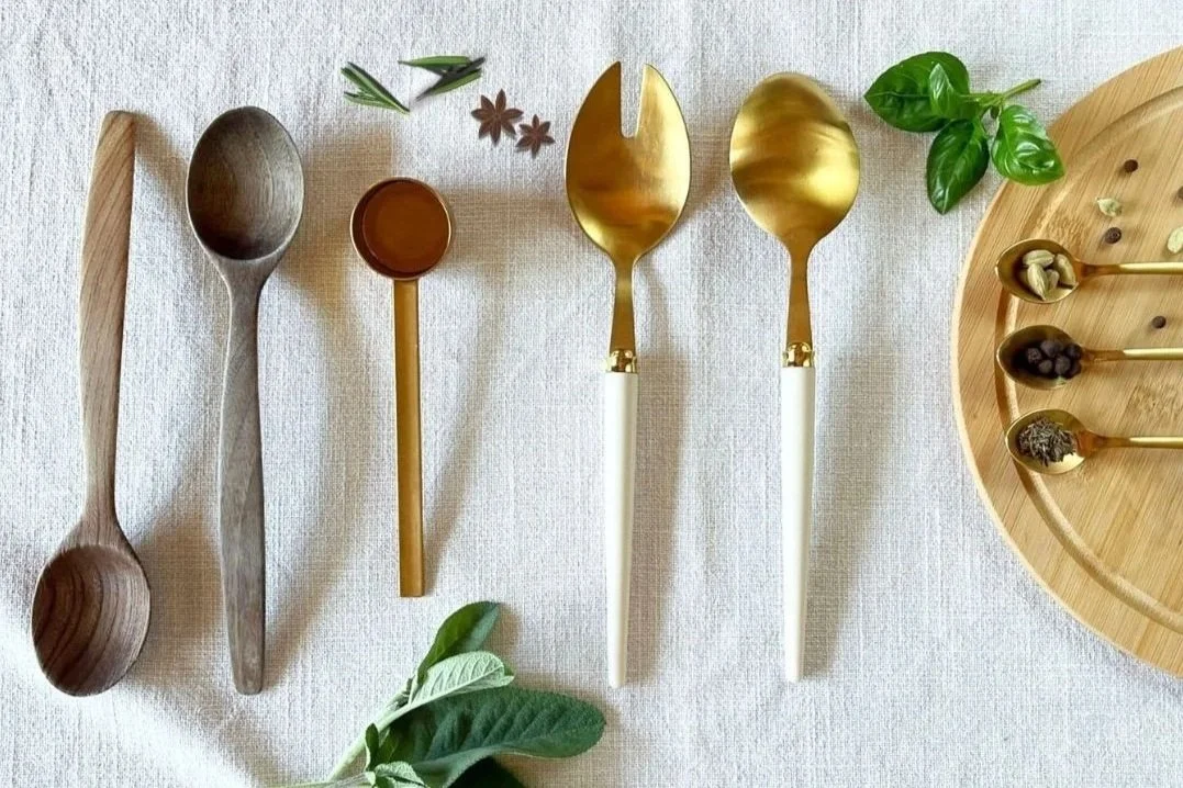 Cutlery in gold and wood displayed facing down on a natural table cloth surrounded by herbs and spices for perfect cooking lifestyle.