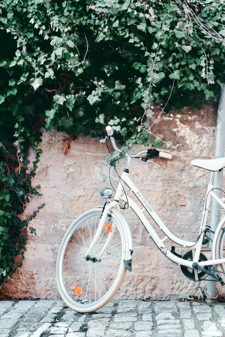 An editorial, minimalist photograph of a classic bicycle resting against a textured historic stone wall in a small European town.