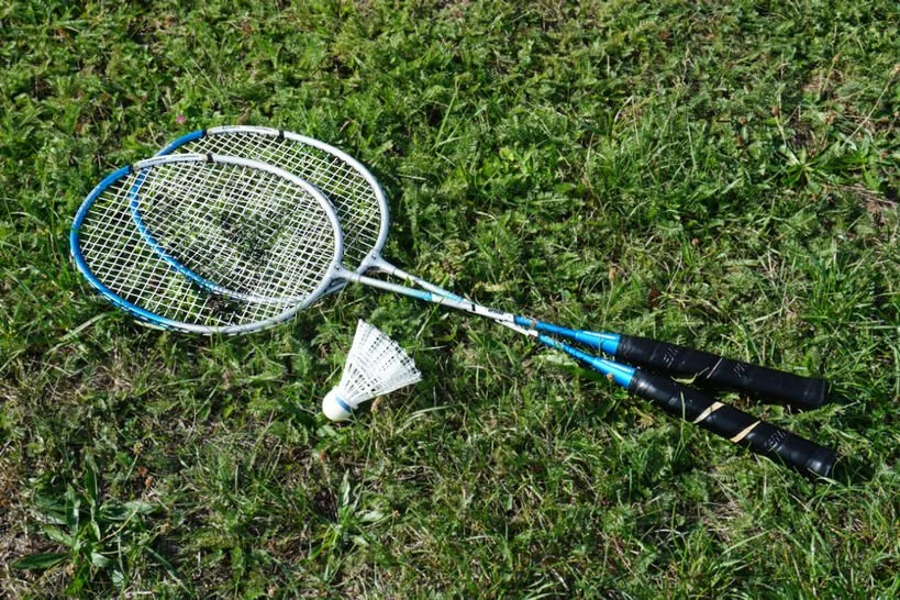 Minimalist wooden badminton rackets lying on fresh green grass, highlighting active family lifestyle and mindful outdoor recreation in a large backyard
