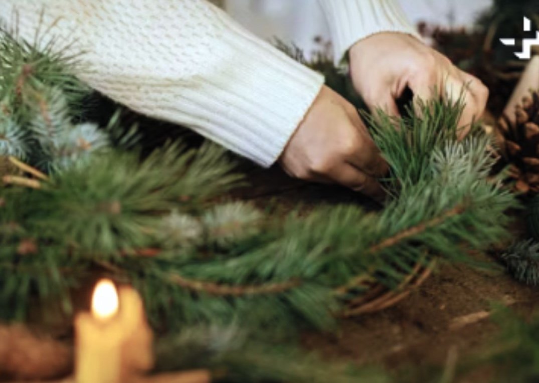 Hands arranging a handmade Christmas wreath with pine, eucalyptus, and natural elements, creating festive decor with a personal touch
