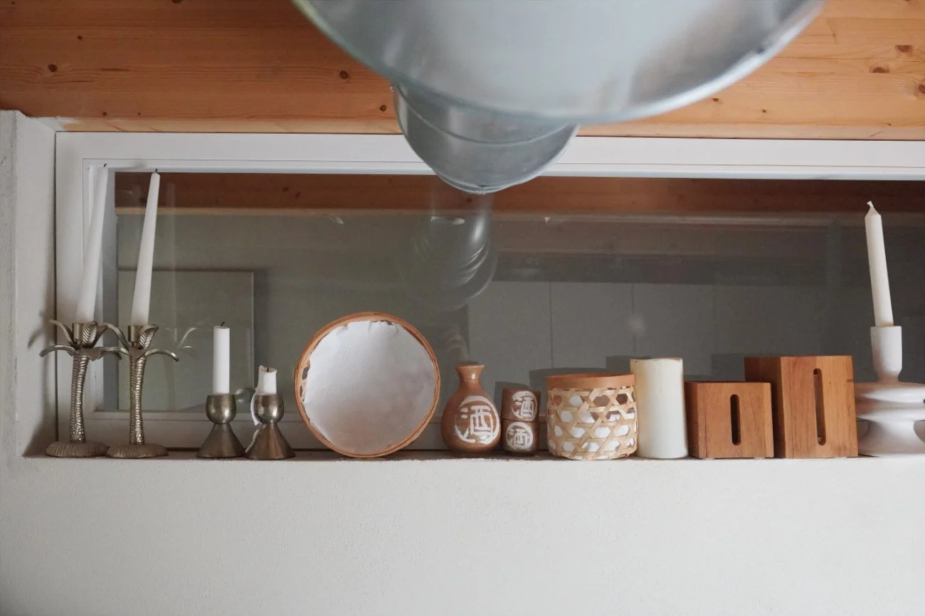 A high narrow transom interior wall window allowing natural light into a small utility room layout, featuring decorative candleholders on a shelf in the foreground.