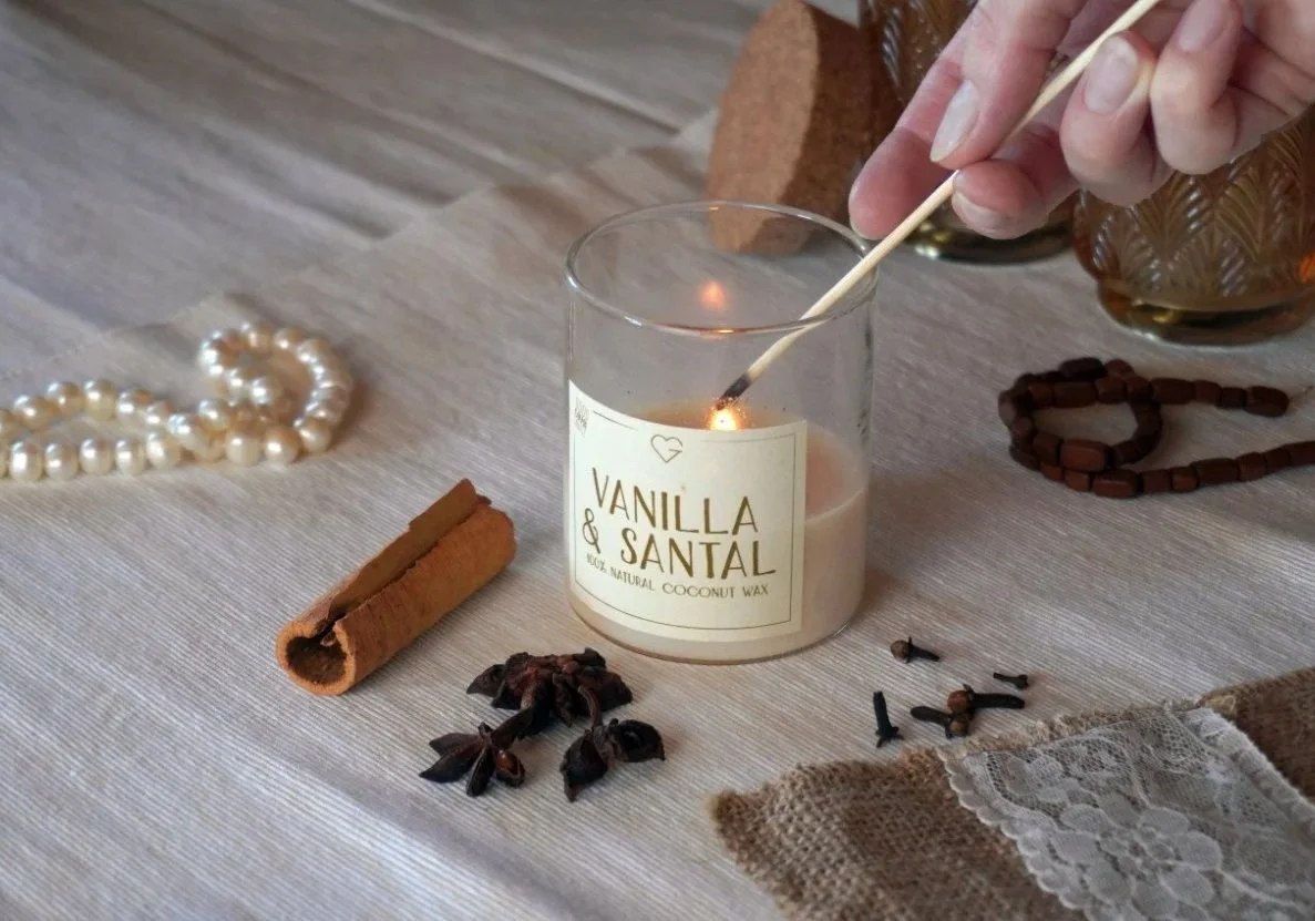 Hand lighting a soy candle surrounded by natural festive decorations, symbolizing holiday rituals and moments of calm.